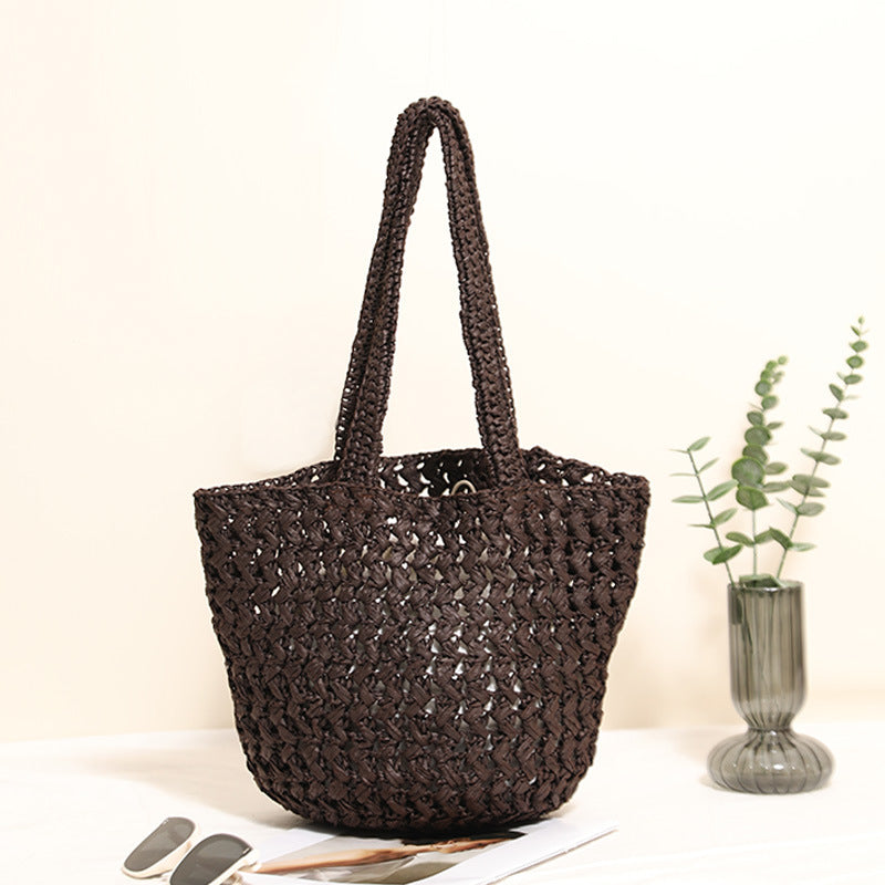 Coffee paper straw shoulder bag standing upright beside a glass vase of eucalyptus