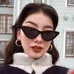Woman wearing black triangular cat eye sunglasses with gray lenses in front of a building
