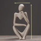 Speckled sandstone abstract resin meditator figurine posed in thought on a dark backdrop