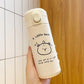 Cream insulated bottle held against a tiled wall, black bear face drawing and A little bear text