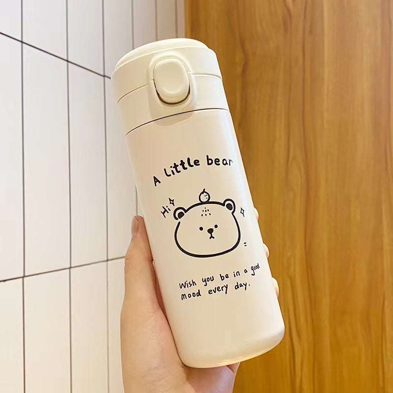 Cream insulated bottle held against a tiled wall, black bear face drawing and A little bear text