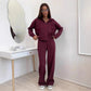 Burgundy zip front hooded sweatshirt and wide leg trousers set worn by a model beside a white console table