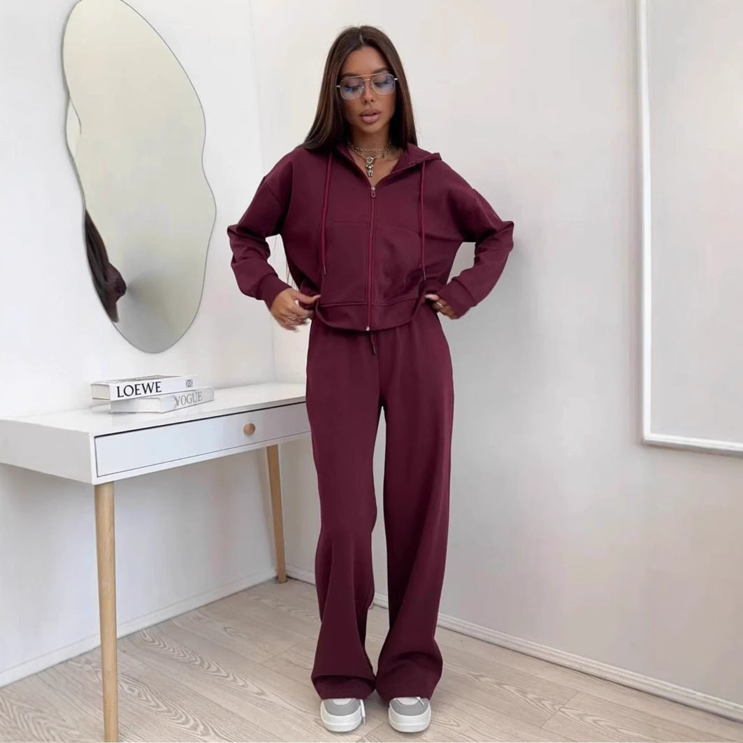 Burgundy zip front hooded sweatshirt and wide leg trousers set worn by a model beside a white console table