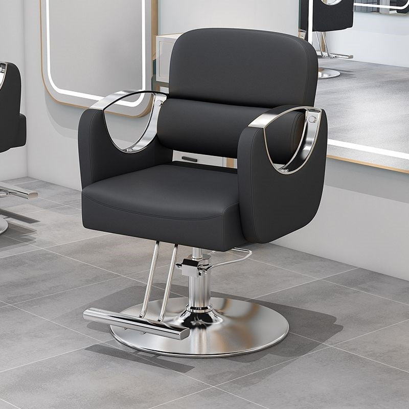 Black salon styling chair with curved gold metal armrests on a gold disc base in a salon