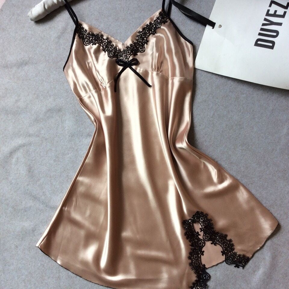 Champagne satin slip nightdress with black lace at the V neckline and a black bow, flat on a gray cloth