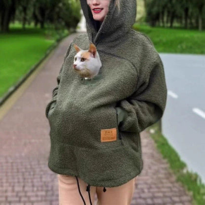 Woman outdoors in an olive green lamb fleece hoodie with a cat looking out of the arched chest pouch