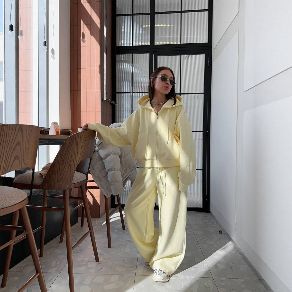 Woman wearing a light yellow hoodie and wide leg trousers set in a bright room, full length view