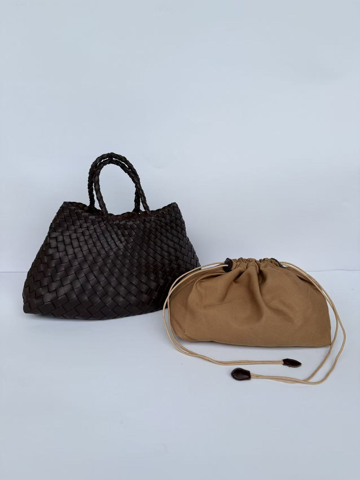 Dark brown woven PU handbag with braided handles beside a tan drawstring pouch
