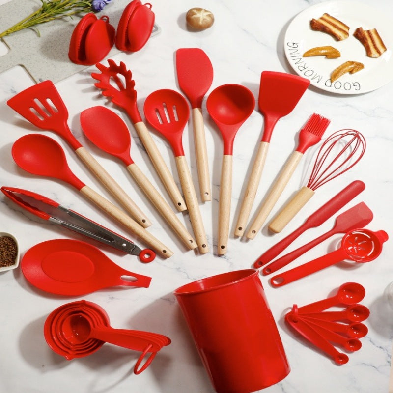 Red silicone kitchen utensil set on a marble counter with the crock, tongs, whisk and measuring cups