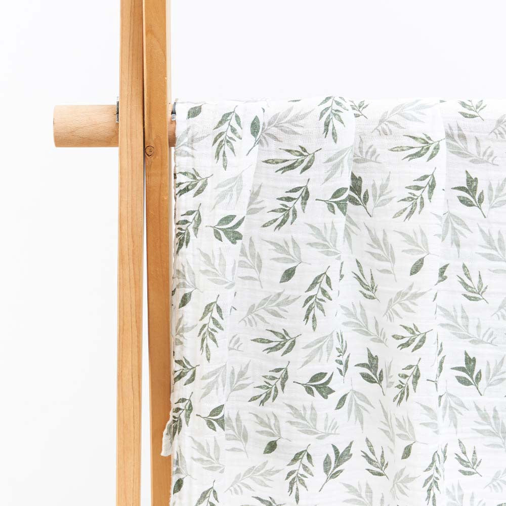 Large cotton muslin gauze baby blanket laid out, showing the loose breathable weave and print