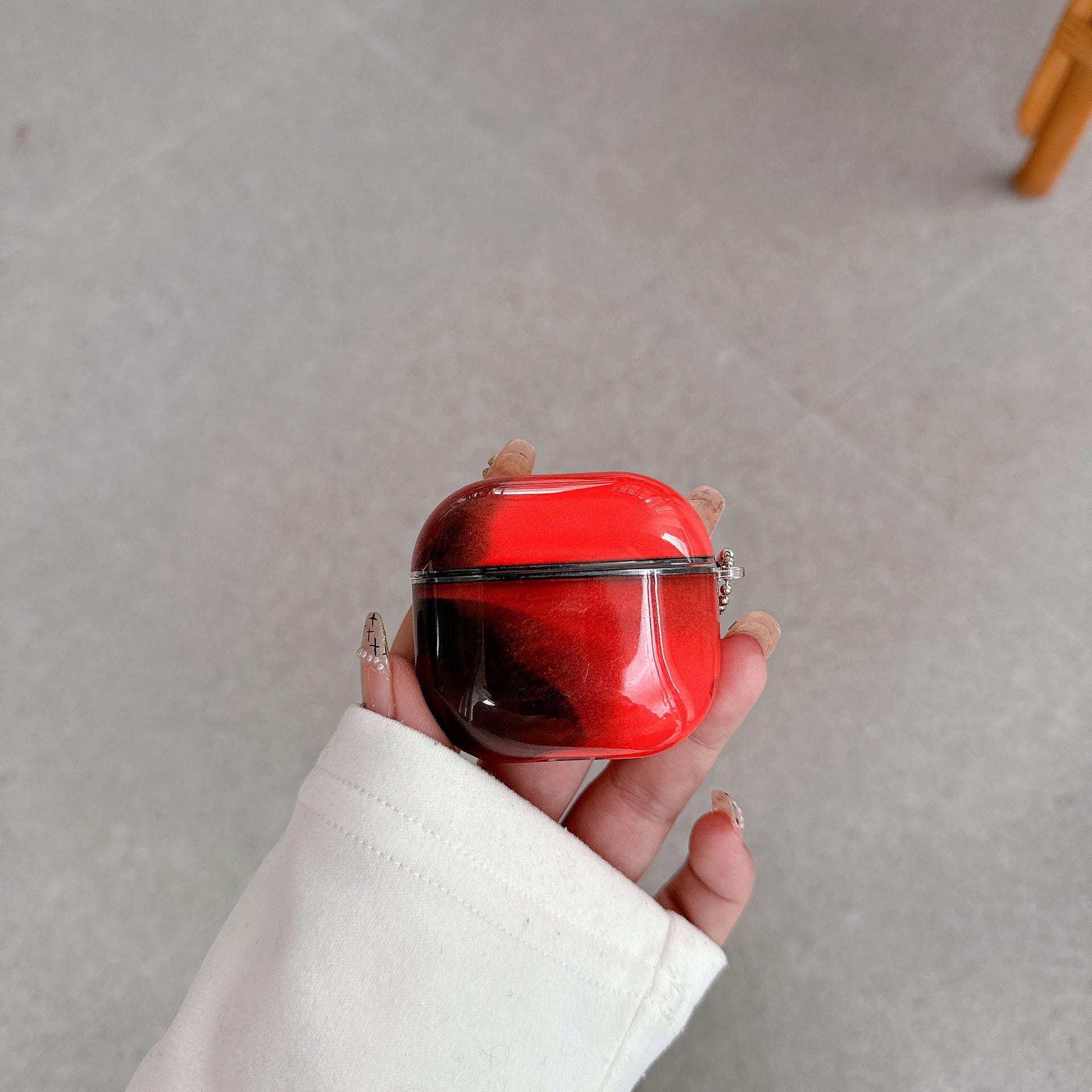 Red marble AirPods cover case held in a hand above a grey floor