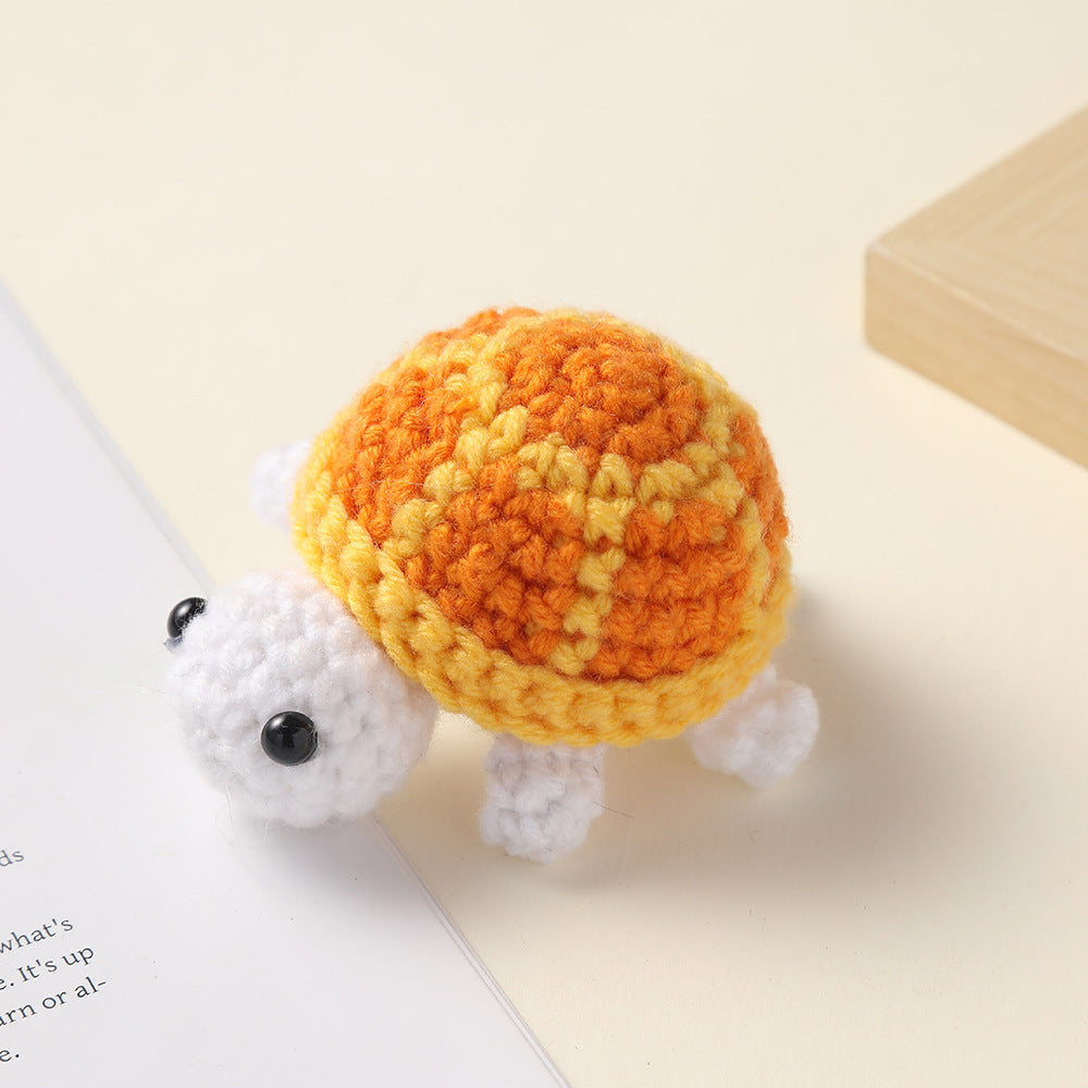 Crocheted orange and yellow shell white turtle, handmade wool charm on a cream surface