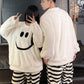 Back of the man's white fleece pullover beside the woman's smiley face top and striped trousers