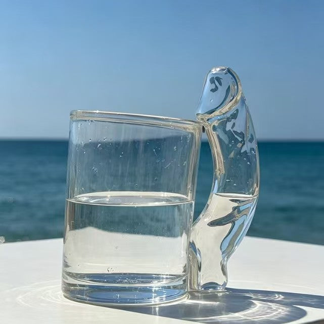 Clear glass novelty mug shown from the side to show the straight cup and sculpted handle