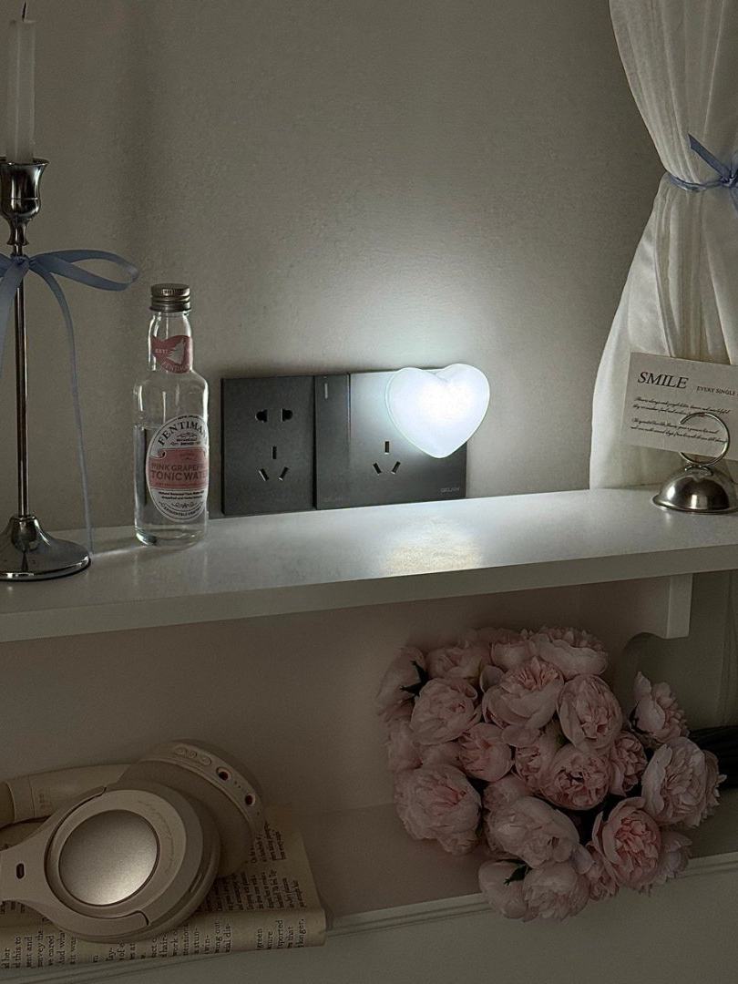 White heart night light glowing softly on a shelf in a dim room