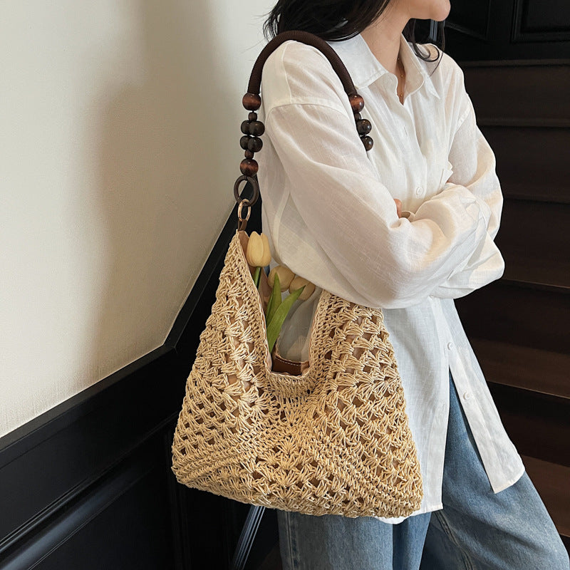 Model carrying a cream open-weave hobo bag on the shoulder by its beaded handle, wearing a white shirt