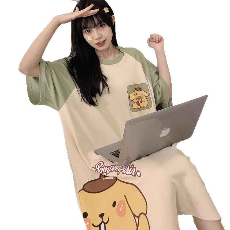 Woman with a laptop on her knees in a cream nightgown with green sleeves, shown on a plain white background