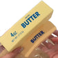 Hand squeezing two yellow butter stick squishy toys in clear bags, showing the printed butter label