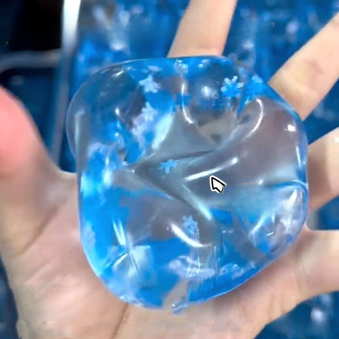 Two blue gel snowflake ice cube squishy toys on a floral background near a hand