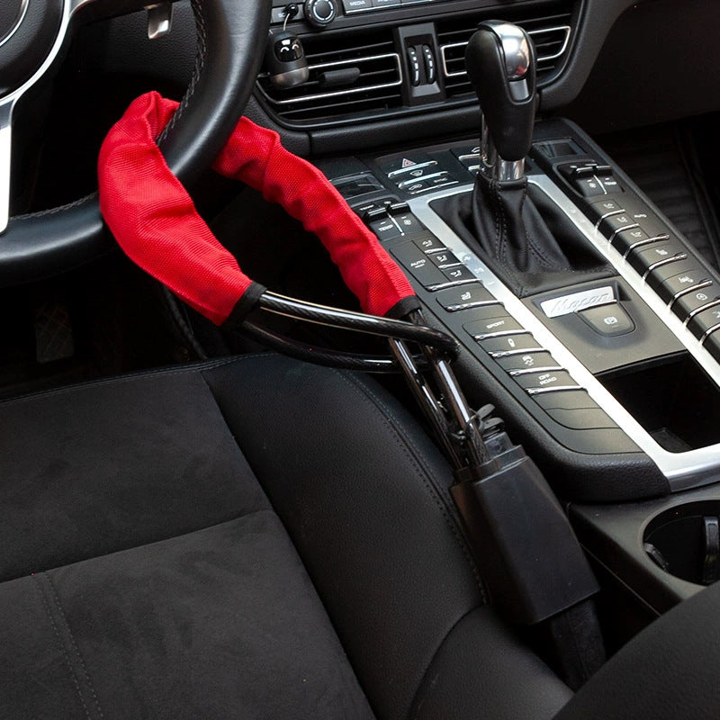 Red sleeved steel cable lock on a steering wheel with its black lock body in the seat belt buckle