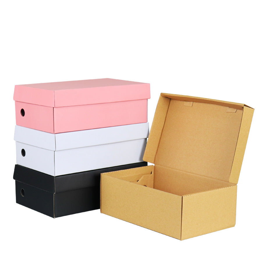 Pink, white and black shoe boxes stacked beside an open kraft shoe box on a white background