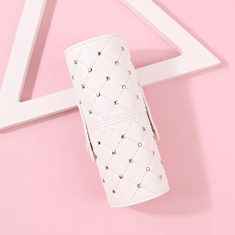 White studded brush holder lying on a pink surface beside a wooden triangle prop, diamond quilting visible