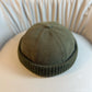 Washed dome beanie with a rolled ribbed knit cuff resting on a soft chair
