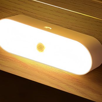 Oval LED motion sensor night light glowing warm yellow on a wall