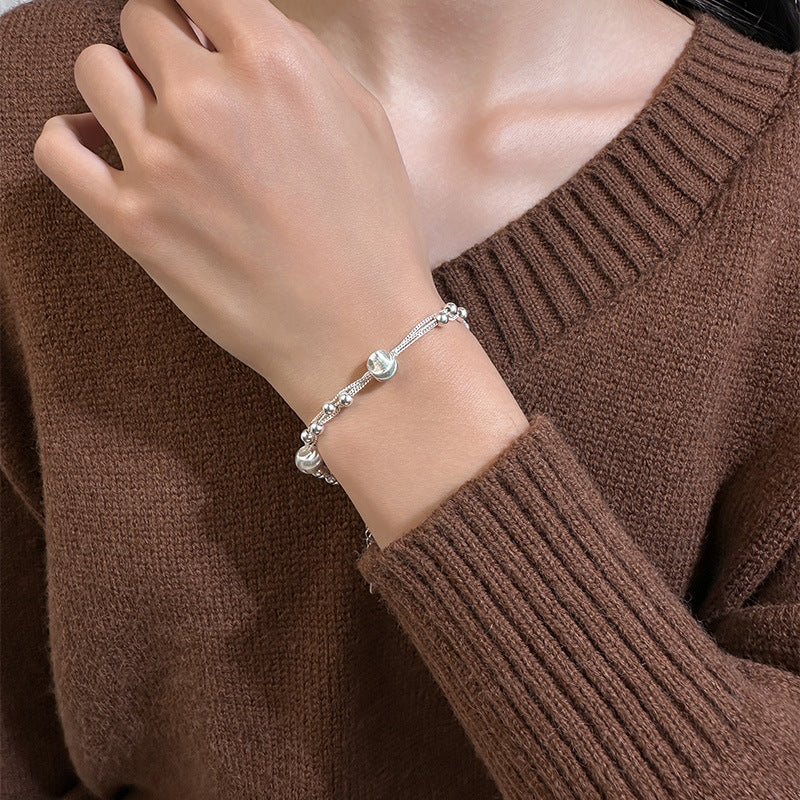 Silver bead bracelet worn on a wrist against a brown knit sweater sleeve