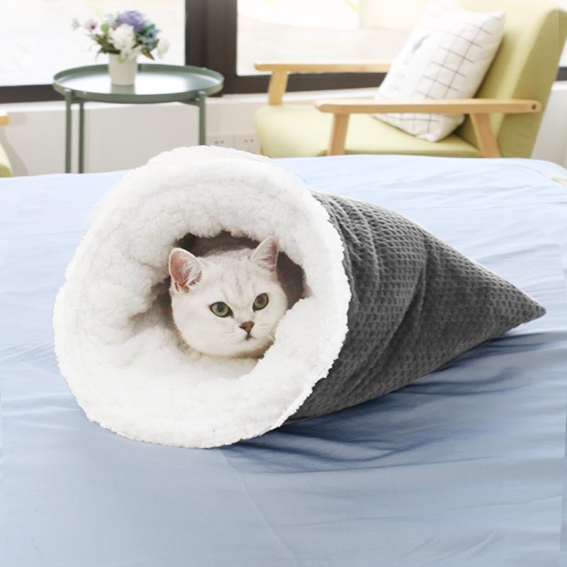 Gray waffle weave cat sleeping bag with plush white fleece lining and a cat resting inside on a bed