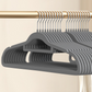 Gray flocked hangers in a row on a rail, close view of the slim shoulder shape