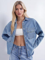 Woman wearing a washed blue denim shirt jacket open over a white top and light jeans with chest pocket and metal buttons