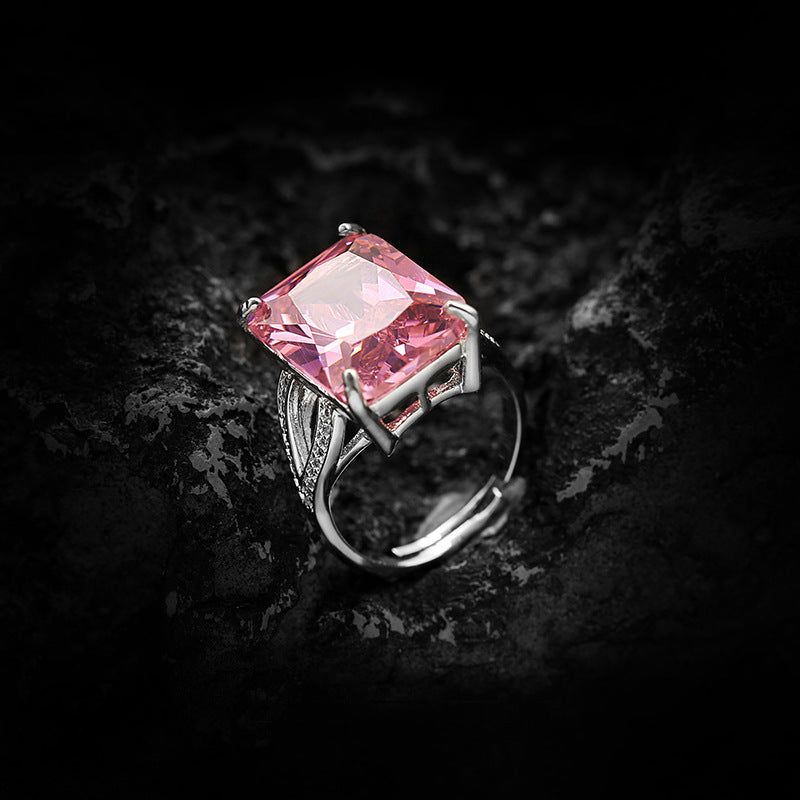 Oversized pink emerald cut simulated diamond on an open adjustable band, photographed on dark rock