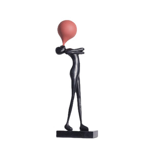 Slim black balloon figure sculpture seen from the side, arms folded and balloon lifted above the tucked in face