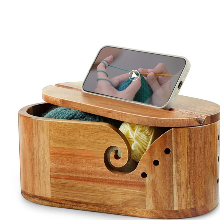 Acacia yarn bowl closed with its lid, a phone standing upright in the groove on top