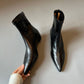 Top view of black pointed toe ankle boots held by hand, showing the back zip and slim pointed toes