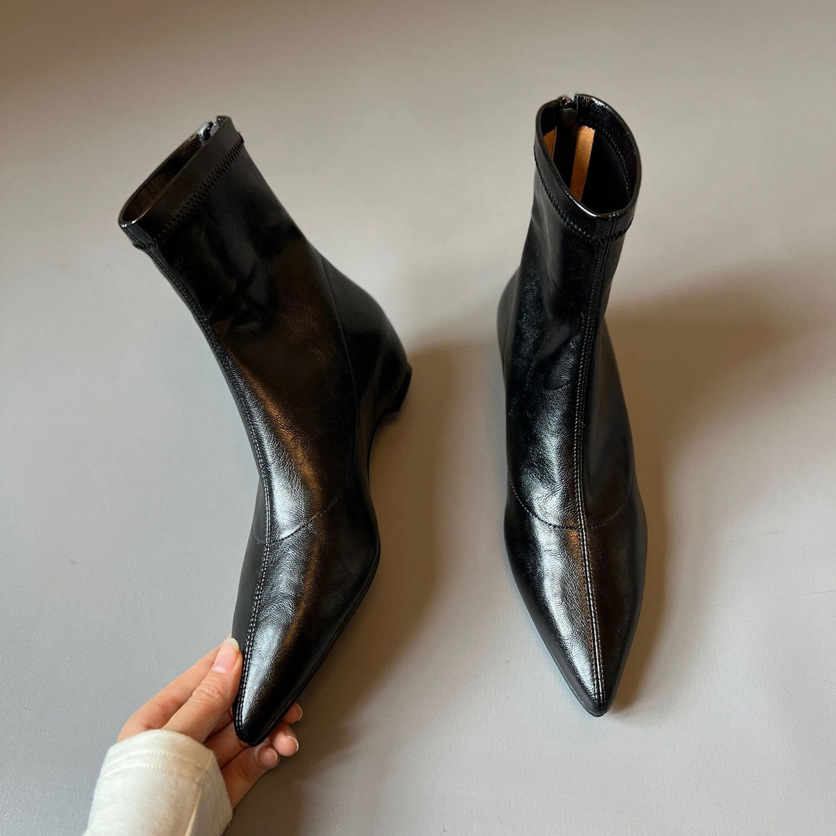 Top view of black pointed toe ankle boots held by hand, showing the back zip and slim pointed toes