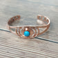 Open copper cuff bracelet on wood, blue centre stone and three flush magnet discs in each end