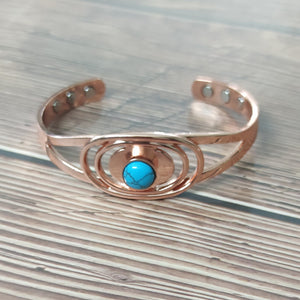 Open copper cuff bracelet on wood, blue centre stone and three flush magnet discs in each end