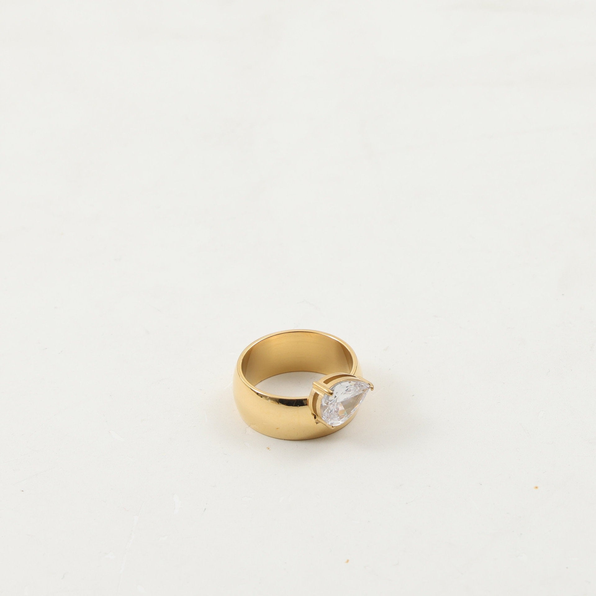 Drop zircon ring shown on a finger for scale next to a slim gold-plated band
