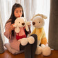 Woman holding a cream plush rabbit in a red outfit beside a larger yellow outfit rabbit by a window