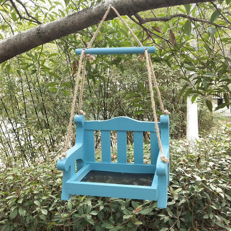 Blue wooden bench shaped bird feeder with a slatted backrest hanging from rope under a tree branch