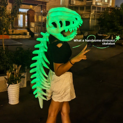 Person wearing a glowing green dinosaur skull mask with a ribbed spine down the back outdoors at night