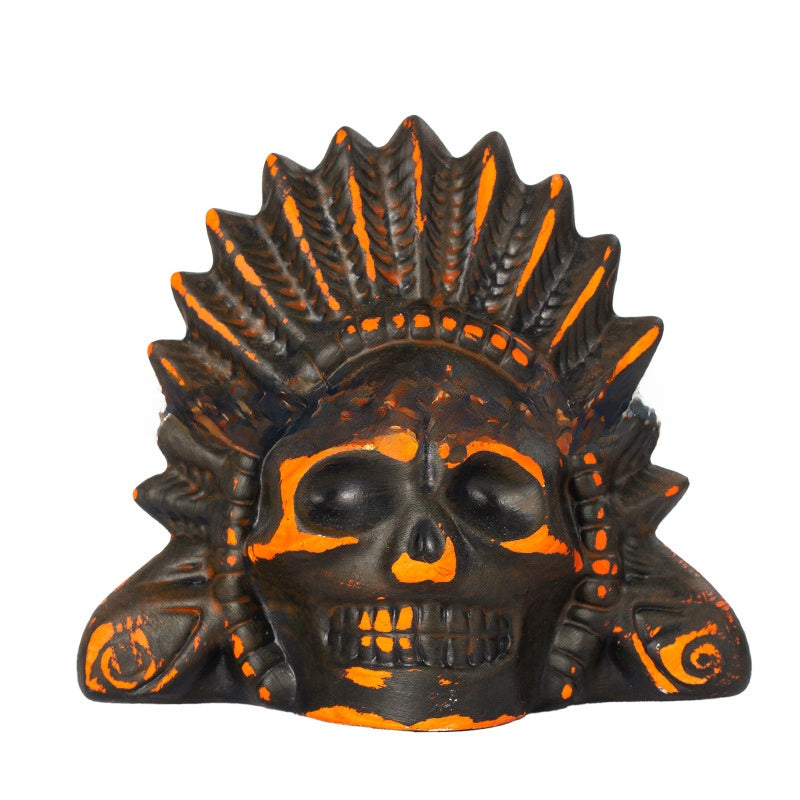 Black ceramic skull death whistle with orange painted feather headdress and eye sockets on a white background