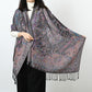 Woman holding open a black paisley jacquard scarf with a multicolor floral pattern and black tassels
