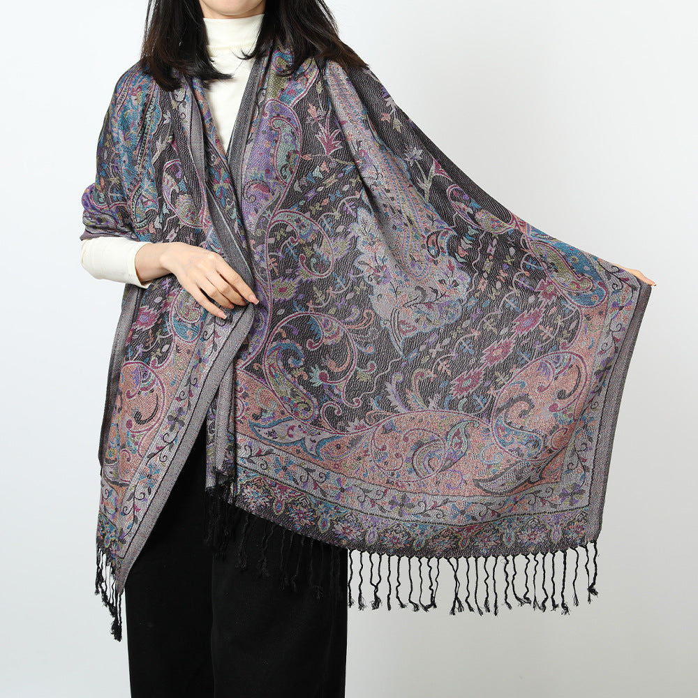 Woman holding open a black paisley jacquard scarf with a multicolor floral pattern and black tassels