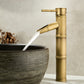 Antique copper bamboo basin faucet pouring a sheet of water into a dark stone vessel bowl