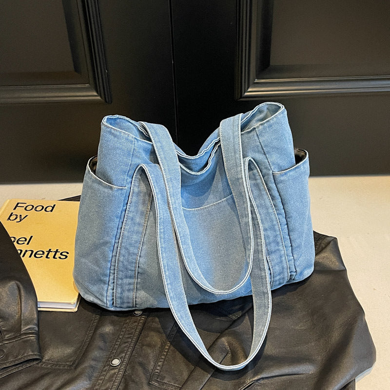 Cowboy light blue denim shoulder tote resting on a leather jacket, faded wash with contrast stitching