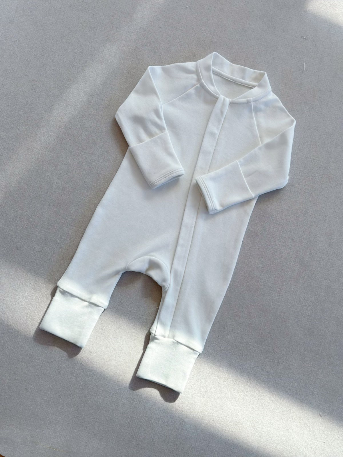 Natural White zip front baby romper laid flat on a gray floor, image of the 90 cm, 18 to 24 months size option