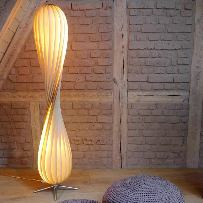 Spiral wood slat lamp lit at night beside a bed giving a warm diffused glow